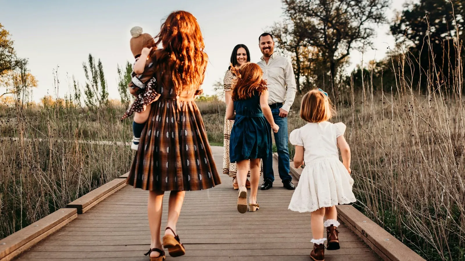 Children running along a wooden boardwalk toward their smiling parents at sunset