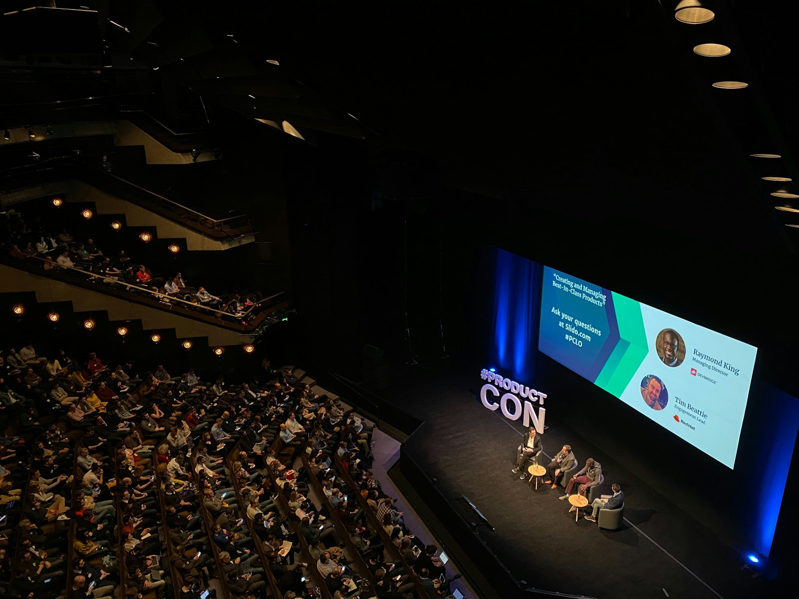 A panel discussion on stage in a large auditorium, with the audience seated in front